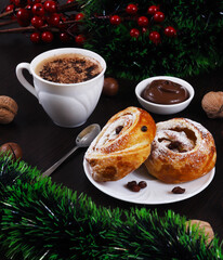 Sweet puff rolls with raisins, with chocolate cream in a white plate and a cup of coppuccino on the Christmas table, New Year. Close-up