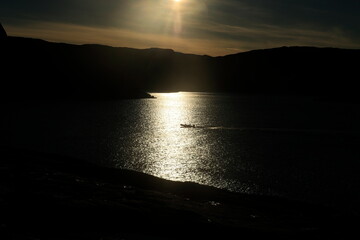 Ein kleines Motorboot fährt in der Abendsonne durch den Lichtschein, das Foto ist stark...