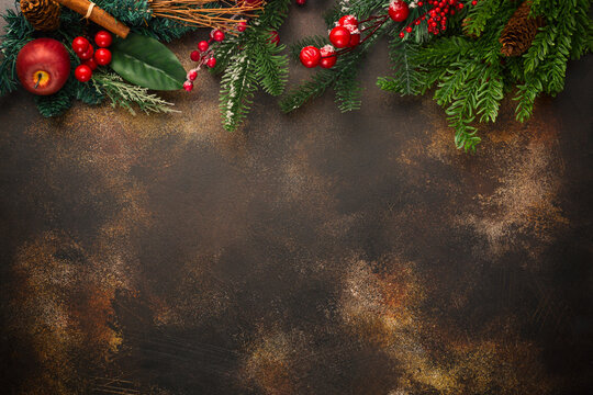 Christmas celebration background. Fir tree branches with cones, red berries and apple on rusty background. Free space