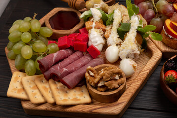 A dish with appetizers of cheese, fruits, vegetables, crackers, meat, berries and nuts