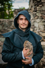A man in medieval clothes against the background of a stone wall of the castle holds a gray rabbit...