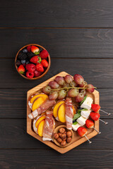 A dish with appetizers of cheese, fruits, vegetables, crackers, meat, berries and nuts