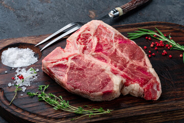 Porterhouse beef steak raw dry-aged on a wooden cutting board with grilling seasonings and a meat fork. Steak on the bone