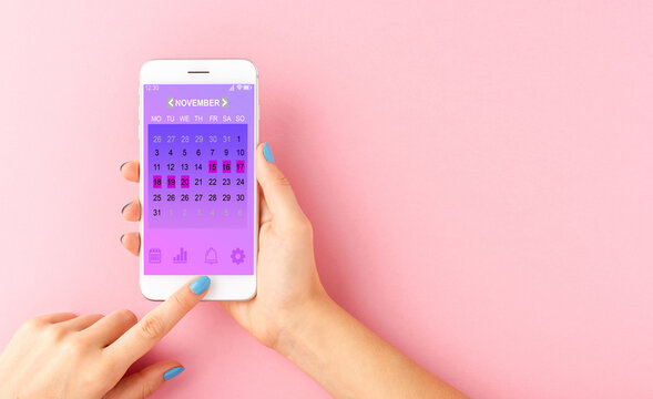 Menstrual cycle tracker mobile app on smartphone screen in woman's hands, graphic representation of period calendar on pink background.