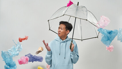 Man with umbrella standing under falling garbage