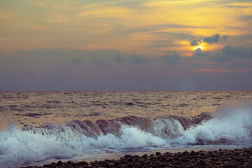 Raging blue sea against backdrop of setting sun in clouds with yellow and blue tones. Landscape of sea and setting sun.