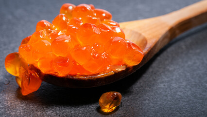 Red caviar on wooden spoon on black table illuminated by white light. Expensive red caviar on spoon.