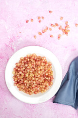 Ripe pomegranate in white plate on pink background