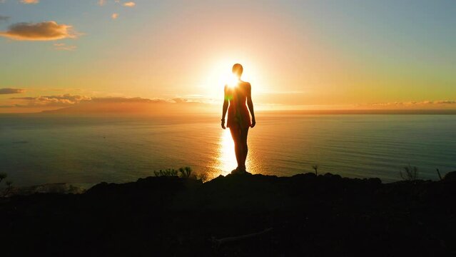 Woman silhouette on mountain top with ocean view at sunset light aerial Tenerife Island. Sunburst rays otline a person. Lonely girl enjoying sunrise. Sunbeams rise from sea.