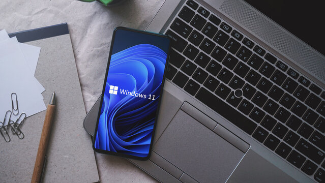 Dobrich, Bulgaria &ndash; 2022, November, 26: Mobile phone on a laptop with the Microsoft logo and Windows 11. Illustrative editorial concept for software technology and Windows 11.