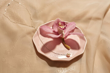 Obraz na płótnie Canvas Chainlet and pink flower on plate on silk cloth