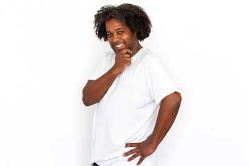 Funny African American man touching chin. Portrait of happy mature male model with dark curly hair in white T-shirt looking at camera, smiling, leaning on hand. Flirt, advertisement concept