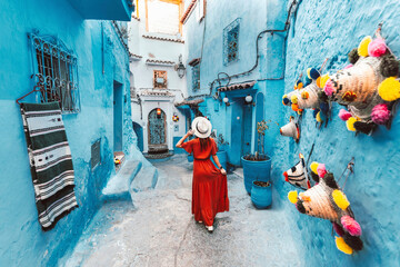 Young woman with red dress visiting the blue city Chefchaouen, Marocco - Happy tourist walking in Moroccan city street - Travel and vacation lifestyle concept - obrazy, fototapety, plakaty