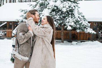 Young couple girl guy walking near barn with skates. Snowy cold winter in countryside. Skating, kissing, having fun, laughing in stylish clothes, fur coat,hat.Romantic love story,village date,weekend