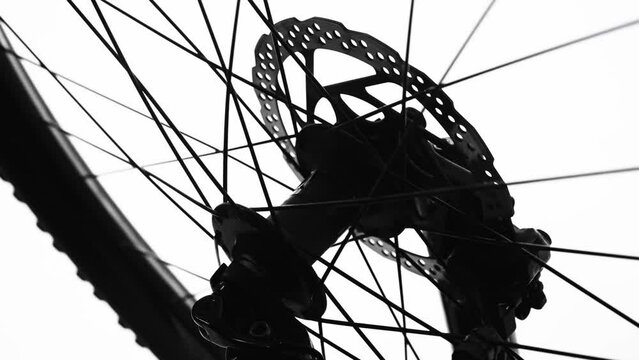 Black silhouette of a bicycle wheel spinning on a white isolated background. Close up of round bike wheel with rubber tread tire, spokes and brake. Rotation of the wheel on a sporty modern bike.