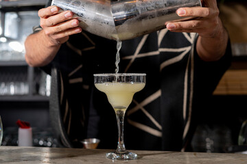 Fototapeta na wymiar Bartender preparando un coctel refrescante margarita de limon usando un boston shaker, con garnitura de limon y sal, servida en un bar 