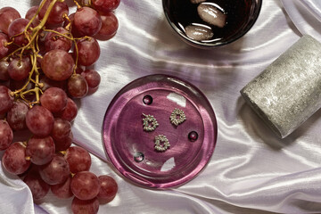 Earrings, candle, grapes and cola on silk cloth