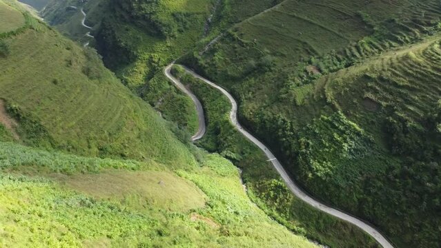 Aerial/Drone shot of an amazing winding road in East Asia near Ha Giang Loop including a road, mountains, grass, valley, cars and motorcycles