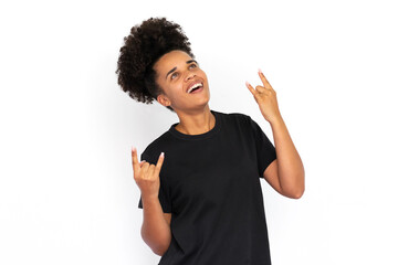 Portrait of cheerful young woman making rock and roll gesture against white background. African...