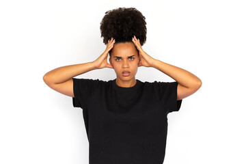 Portrait of outraged young woman holding head in hands. African American woman wearing black T-shirt looking at camera in indignation. Irritation concept