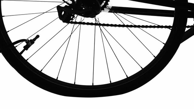 Inflating the rubber tread tire of a bicycle wheel with a pump. Close up of the black silhouette of a wheel filling with air. A mans hand disconnects the pump and twists the nipple on bicycle wheel.