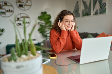 Smiling young woman student wearing headphones using laptop elearning or remote working at home...
