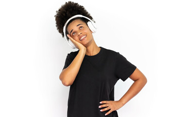 Fototapeta na wymiar Happy young woman listening to music leaning head on hand against white background. Portrait of African American woman wearing black T-shirt posing in headphones. Music and leisure concept