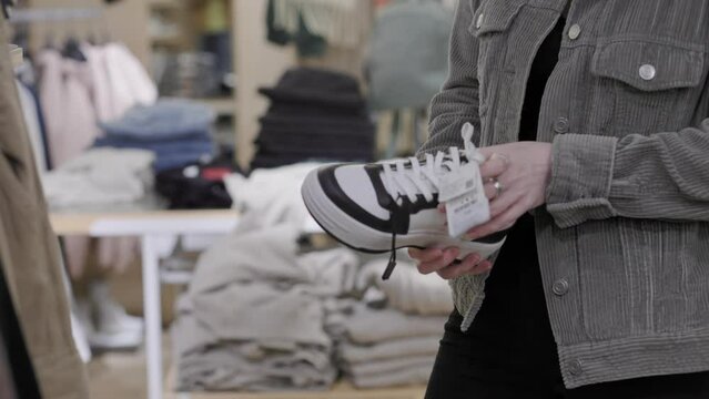 Woman holds leather sneakers and examining their. Hands and shoes close-up. Concept of shopping and consumerism.