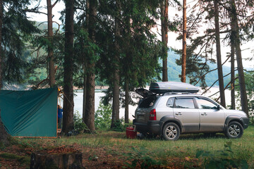Camp, camping in wilderness. Travel and tourism by car. Vehicle near tall coniferous trees. Tents and active recreation in the Carpathian Mountains