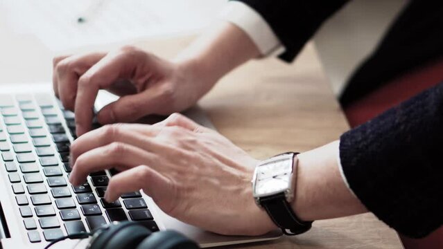 Businessman in a suit and a watch on his arm typing a letter or resume. Close-up of his hands on his desk in the office