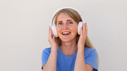 Close-up of ecstatic young woman listening to music in headphones. Caucasian female model with blonde hair and blue eyes in blue T-shirt smiling and enjoying music. Lifestyle, music concept