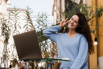 Happy girl chatting and gesticulates with family and friends via video call outdoor in cafe....