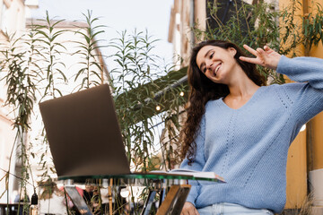 Happy girl chatting and gesticulates with family and friends via video call outdoor in cafe....