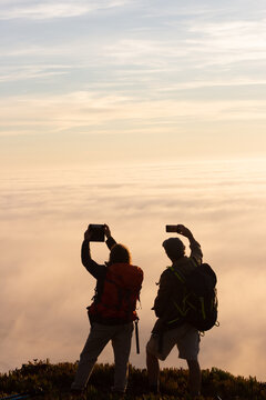 Silhouetted hikers at sunset with phones. Man and woman with backpack taking pictures with mobile phones. Hobby, nature, leisure, friendship concept