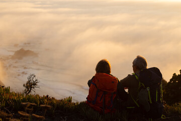 Caring hikers at sunset. Man and woman in casual clothes and with ammunition sitting at peak, looking at setting sun. Hobby, active lifestyle, love concept