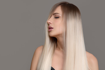 Portrait of a sensual beautiful woman with hair and makeup. Blonde woman with long straight hair on a gray background