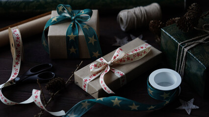 Gift boxes tied with beautiful ribbons with pattern stars with bow.Rolls wrapping paper,ribbons,rope,scissors,cones,red balls old wooden background.Preparing Christmas,New Year holidays,gift wrapping.