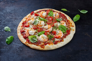 Traditionelle italienische Pizza frutti di mare Riesengarnelen, Tomaten und Mozzarella serviert als close-up auf einem rustikalen schwarzen Board 