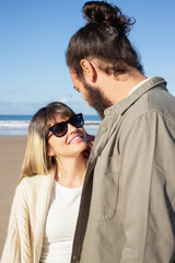 Affectionate couple walking on beach. Bearded man and woman in glasses looking at each other, boyfriend touching girlfriends cheek tenderly. Love, vacation, affection concept