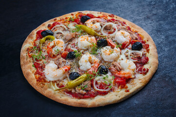 Traditionelle italienische Pizza frutti di mare Riesengarnelen, Tunfisch und Oliven serviert als close-up auf einem rustikalen schwarzen Board 