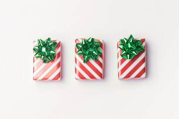 Christmas presents and new year gifts in red striped wrapping paper with green bows on white background with copy space.