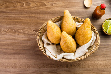 Chicken Coxinha, known as Coxinha in Brazil. Served in the basket, with spices such as lemon and pepper on the side. Wooden table in the background. Traditional brazilian snack Selective focus