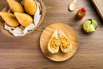 Chicken Coxinha, known as Coxinha in Brazil. Served in the basket, with spices such as lemon and pepper on the side. Wooden table in the background. Traditional brazilian snack Selective focus