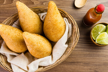 Chicken Coxinha, known as Coxinha in Brazil. Served in the basket, with spices such as lemon and pepper on the side. Wooden table in the background. Traditional brazilian snack Selective focus