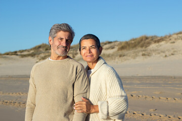 Obraz premium Senior couple spending time outside at seashore together, enjoying warm evening sun. Short-haired lady holding mans hand and smiling while handsome bearded man looking at camera. Relationship concept