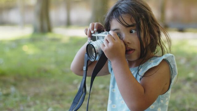 Portrait of happy Asian little girl taking photos with camera. Toddler girl wearing blue dress learning to take photos outdoors. Childhood and photography concept