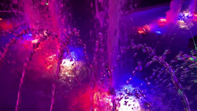 Beautiful multi-colored luminous singing fountain with jets and splashes of water illuminated at night