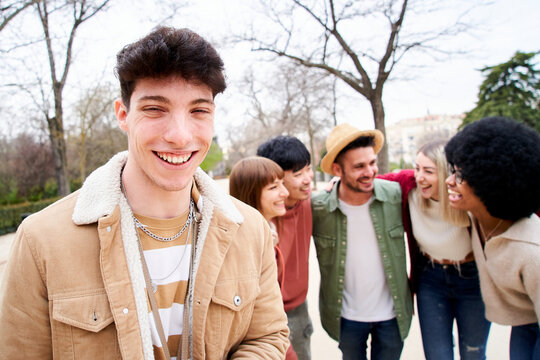 Young smiling guy looking at the camera outdoors with group of friends. Happy people having fun together Focus on a handsome young man. University Colleagues at campus. High quality photo