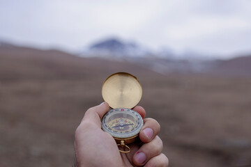 Holds a compass against the backdrop of a mountain