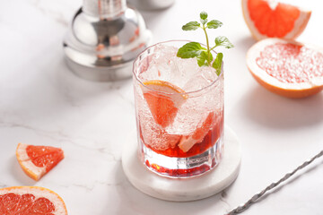 Preparation of a grapefruit alcohol free cocktail - A tumbler glass with ice cubes on marble surface with fresh mint surrounded by steel cocktail shaker and bar equipment